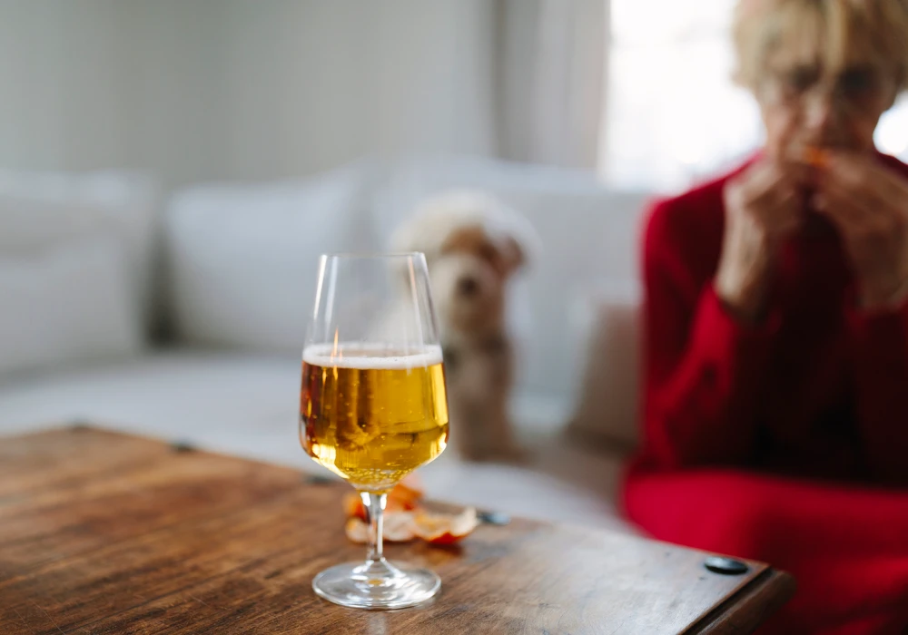 En äldre kvinna sitter vid ett bord med ett glas öl.