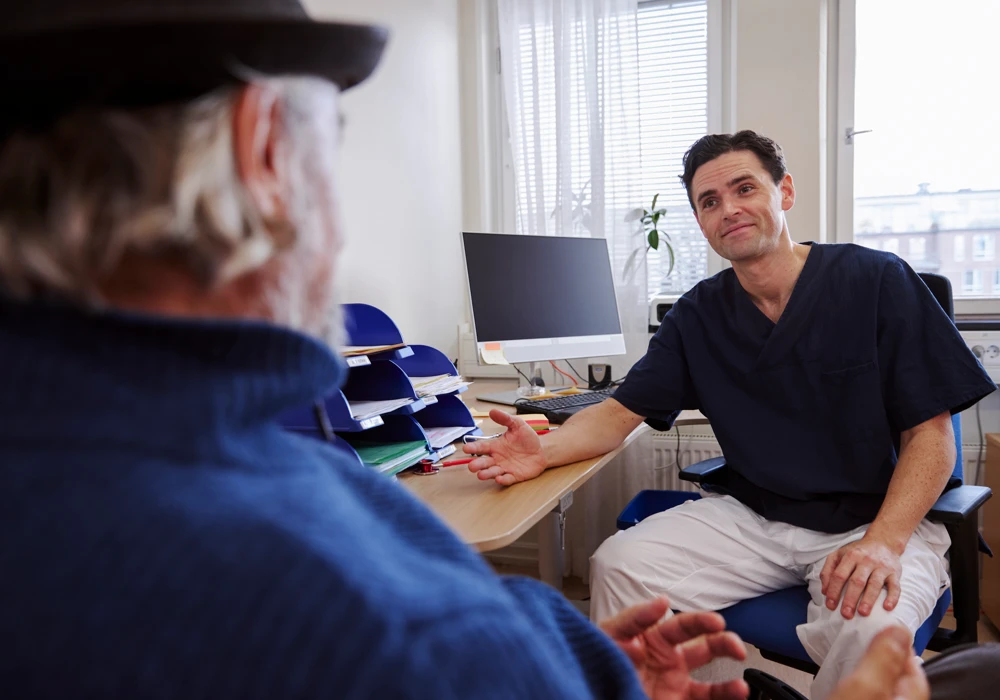 Vårdpersonal med vänligt kroppsspråk i samtal med patient.