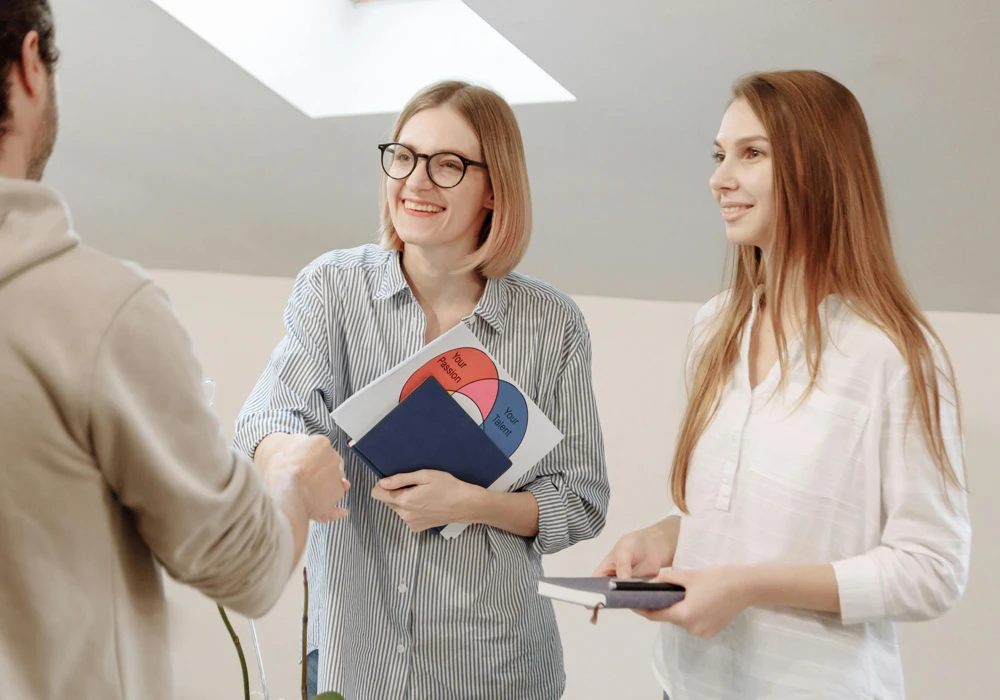 Två personer tar leende emot en tredje för onboarding som nyanställd.