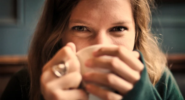 En kvinna håller en kaffekopp med två händer nära ansiktet.