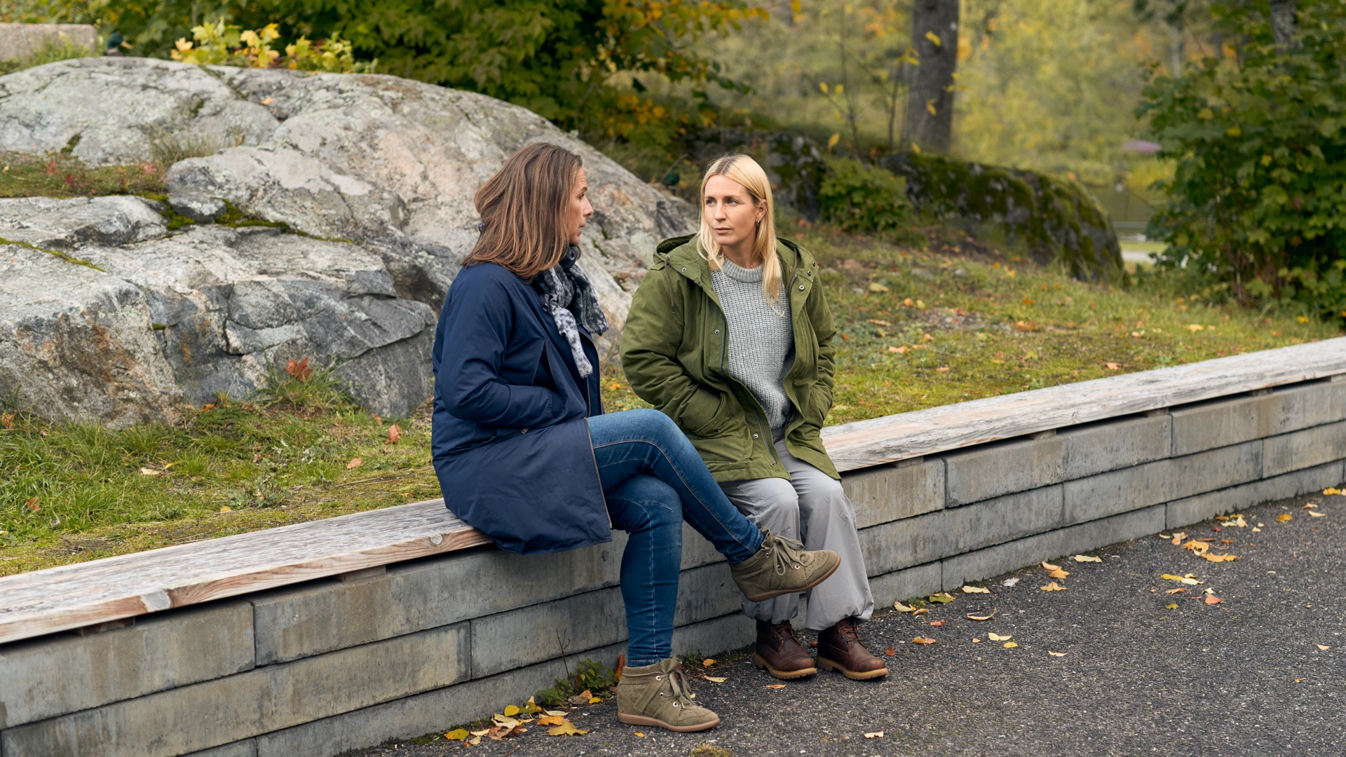 Två kvinnor sitter på en mur och pratar utomhus.