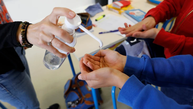 en hand sprutar desinfektionsmedel på en annan hand i skolmiljö.