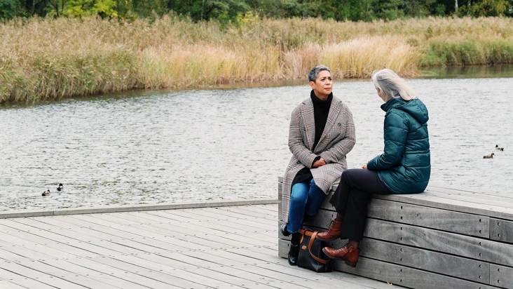 Två kvinnor sitter på en brygga intill ett vattendrag.