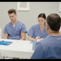 Tre personer, vårdpersonal, sitter runt ett bord. 