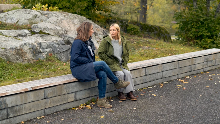 Två kvinnor sitter på toppen av en stenmur och pratar.