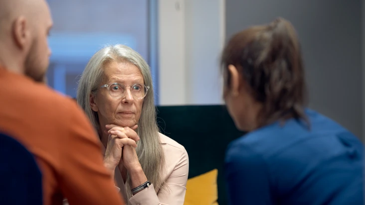 Tre personer sitter vid ett bord och pratar med varandra.