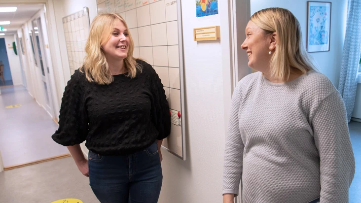 Två kvinnor står och pratar i en korridor.