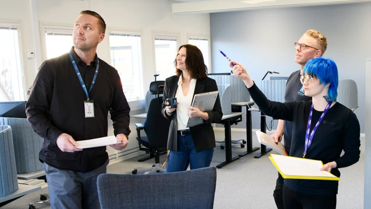 fyra personer i ett kontorslandskap, som pekar och tittar på något utanför bilden.
