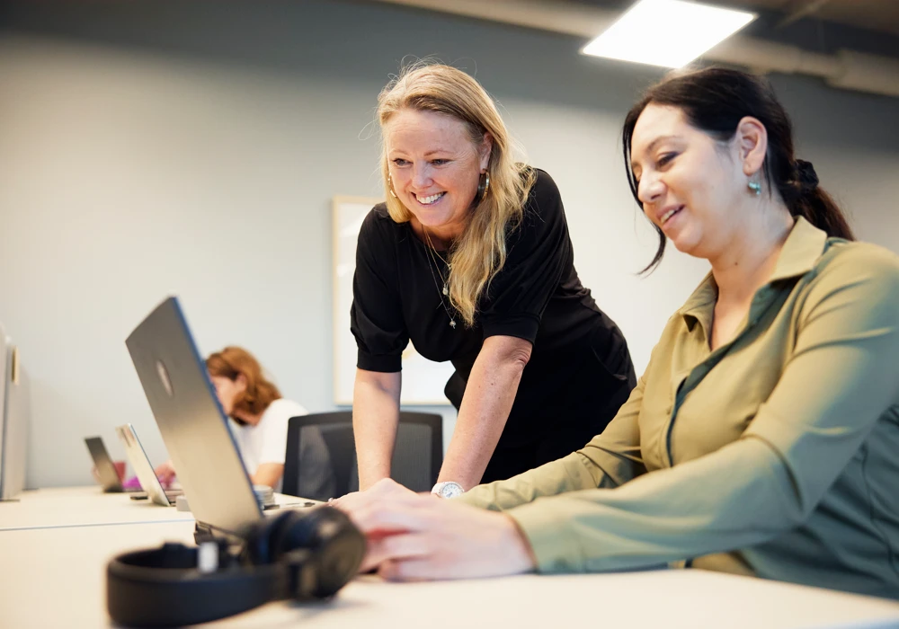 Två kvinnor samarbetar vid skrivbord på ett aktivitetsbaserat kontor.