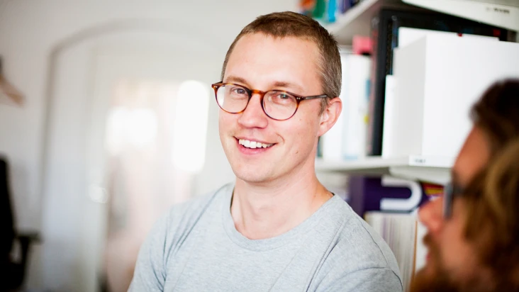 ung man i glasögon och grå tröja i någon typ av lagermiljö.