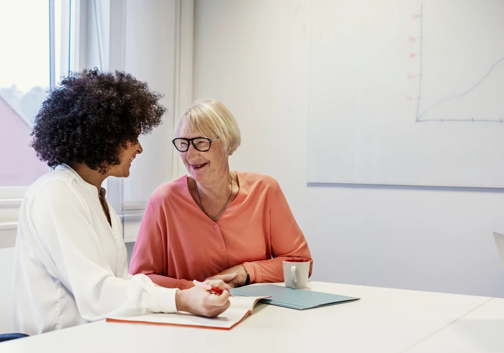 Två kvinnor sitter vid ett bord och pratar med varandra.