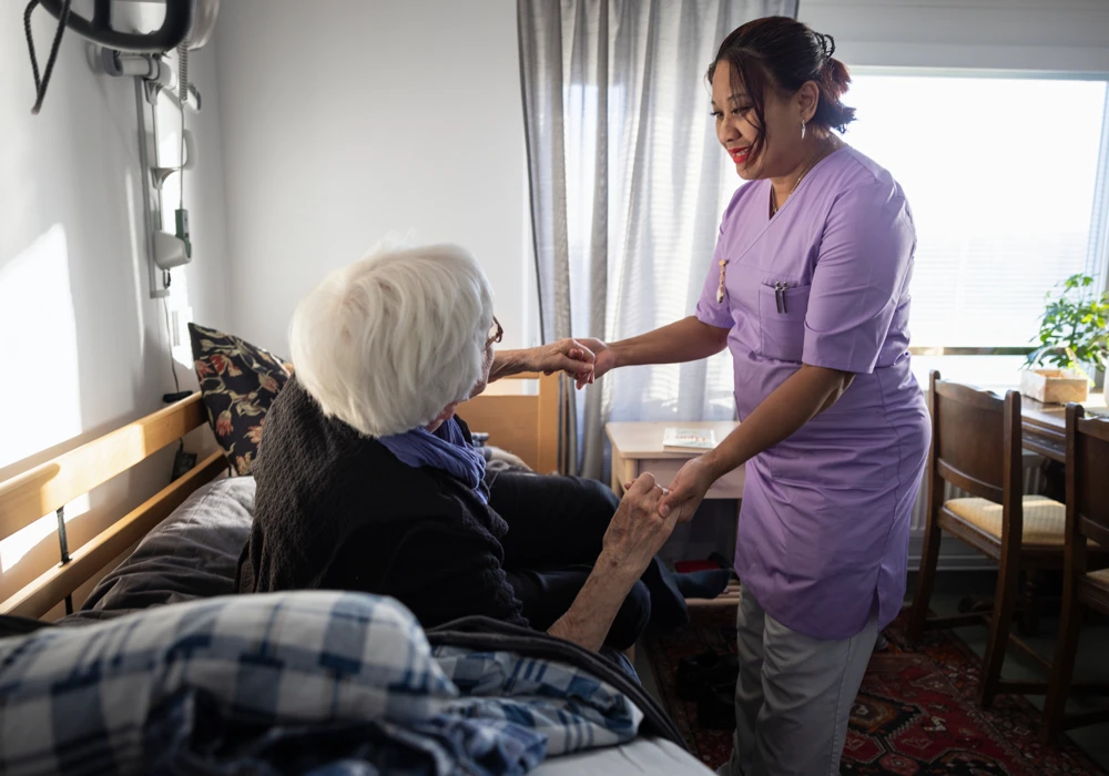 Vårdpersonal hjälper äldre kvinna att komma upp ur sängen.