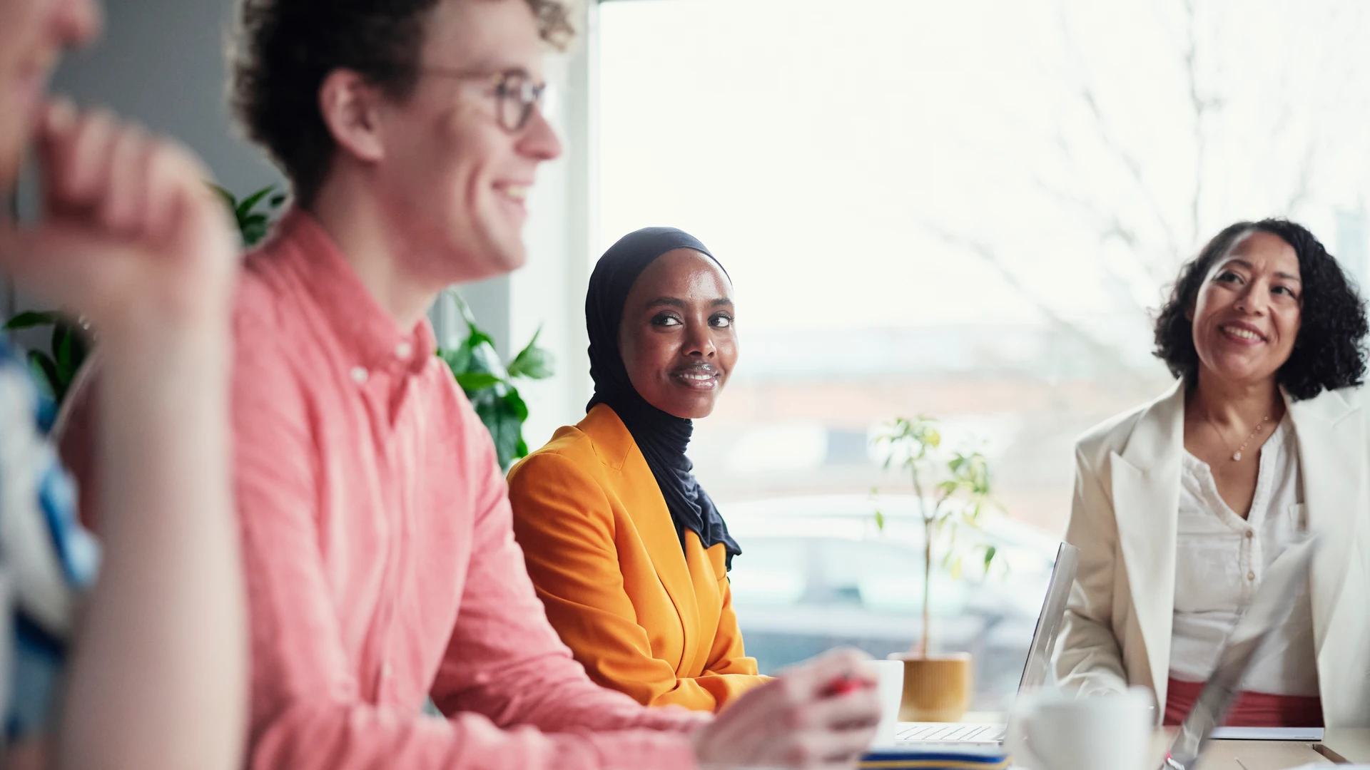 Tre personer har m&ouml;te runt ett kontorsbord i ett kontorsrum. De tittar p&aring; varandra, samtalar och ler.