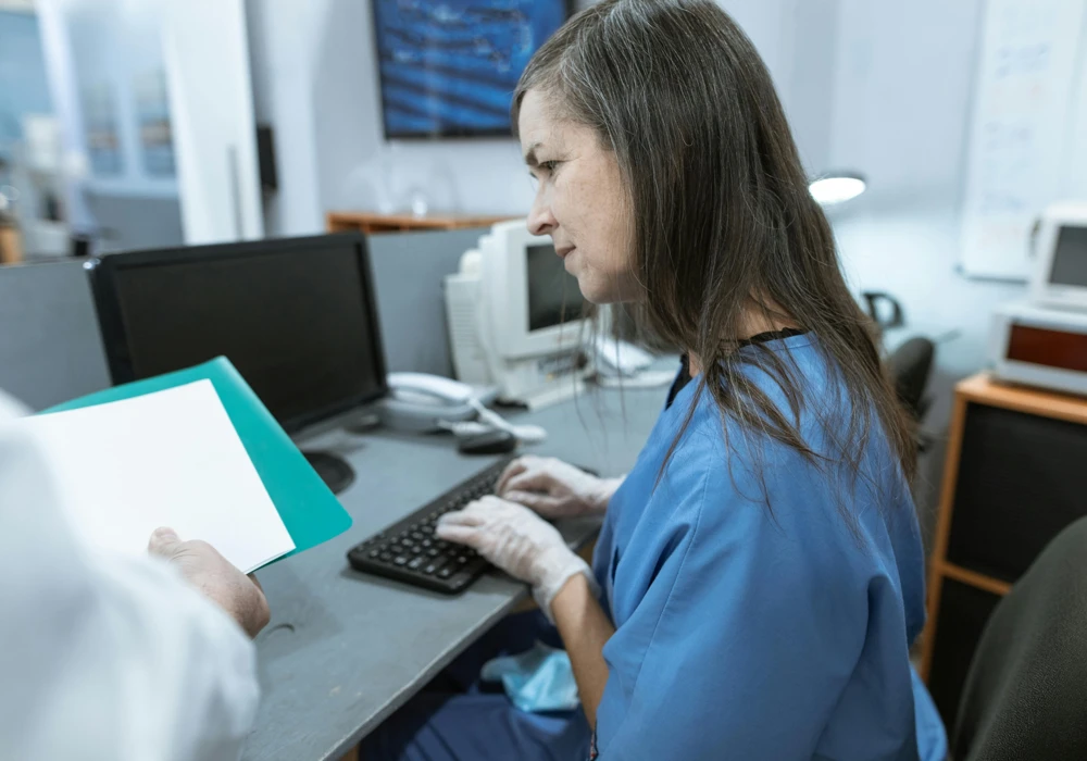 Kvinna vid skrivbord använder en dator och får samtidigt fler papper att hantera.