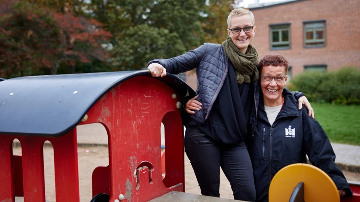 Tv&aring; kvinnor st&aring;r p&aring; en lekplats och tittar mot kameran.