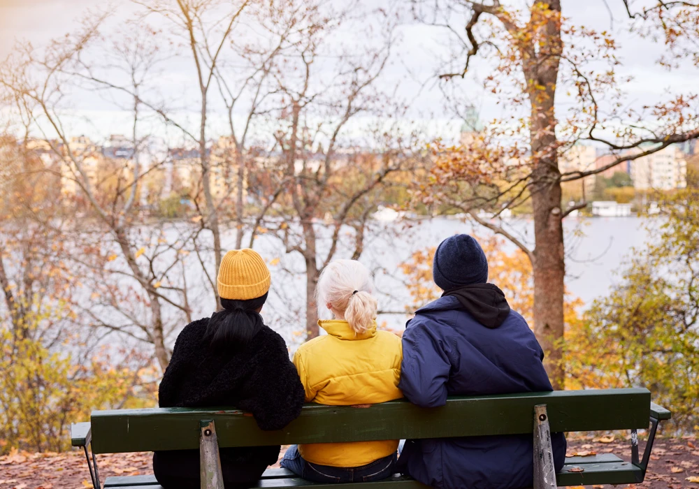 Tre personer sitter på en bänk och tittar på vattnet.