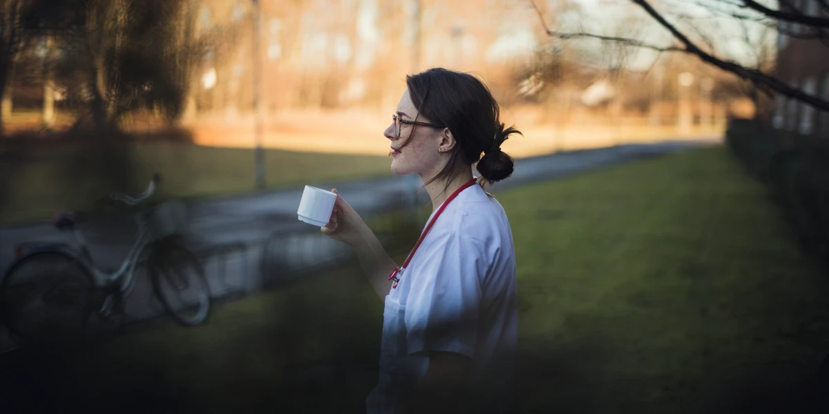 En l&auml;kare dricker en kopp kaffe utomhus.