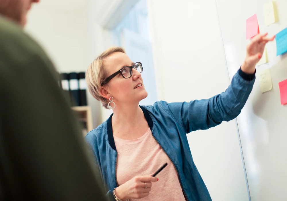 En kvinna i ett möte om implementering sätter post-it-lappar på en vägg.