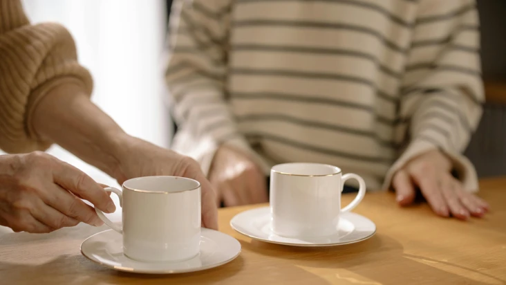 tv&aring; kaffekoppar i f&ouml;rgrunden och en kvinna i randig tr&ouml;ja i bakgrunden.