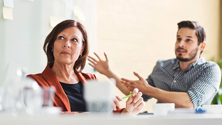 en kvinna och en man p&aring; ett m&ouml;te sitter vid ett bord. De ser b&aring;da p&aring; n&aring;gon utanf&ouml;r bilden.
