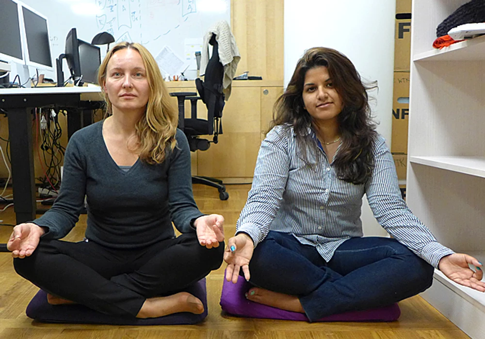 Två personer sitter med benen i kors och mediterar i ett kontorsrum.