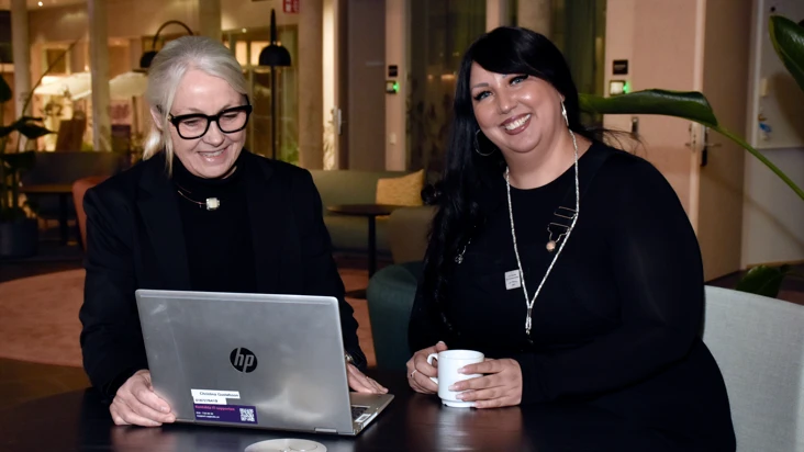 Tv&aring; kvinnor p&aring; bilden sitter vid ett m&ouml;rkt bord i kontorsmilj&ouml;, och tittar p&aring; en dator tillsammans. personerna &auml;r Christina Gustafsson och G&uuml;lperi Saritas.