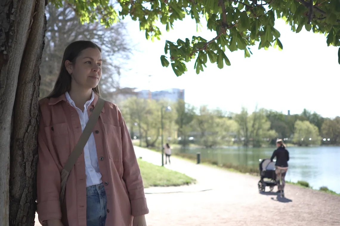 En kvinna som st&aring;r bredvid ett tr&auml;d i en park.