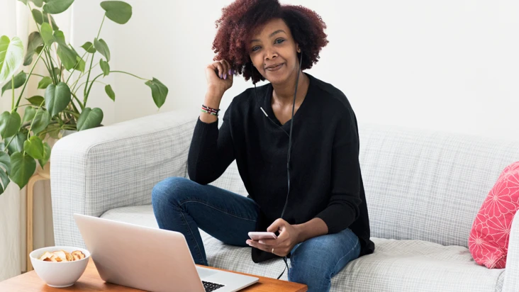 En kvinna sitter p&aring; en soffa och pratar i mobiltelefon.