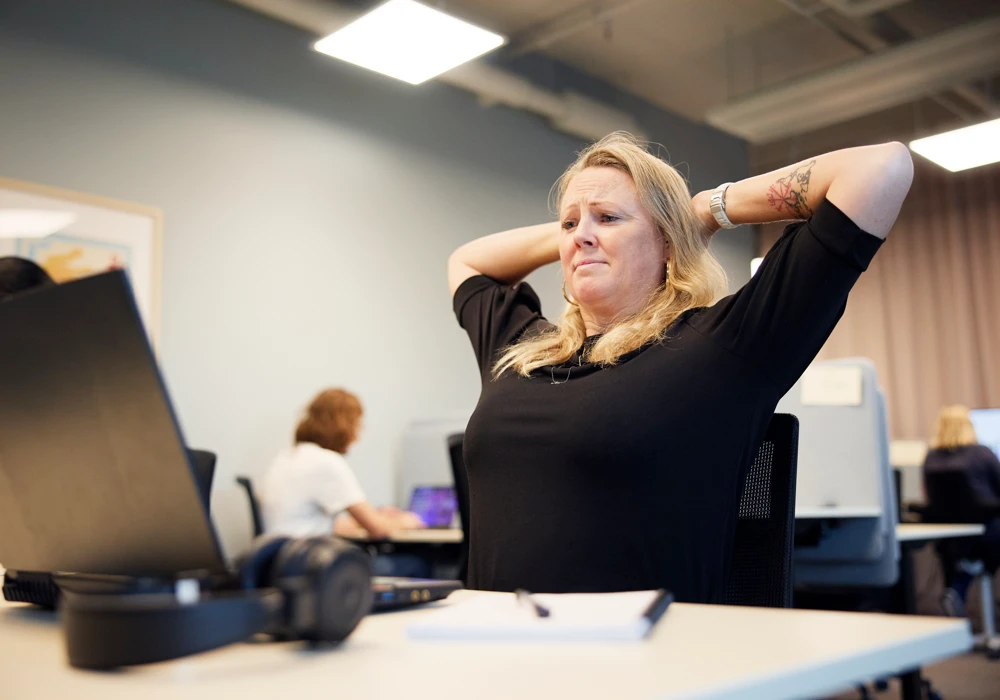 Kvinna sitter vid laptop vid skrivbord och rynkar pannan, tema synergonomi.