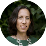 En kvinna i grön klänning mot bakgrund av gröna buskar.