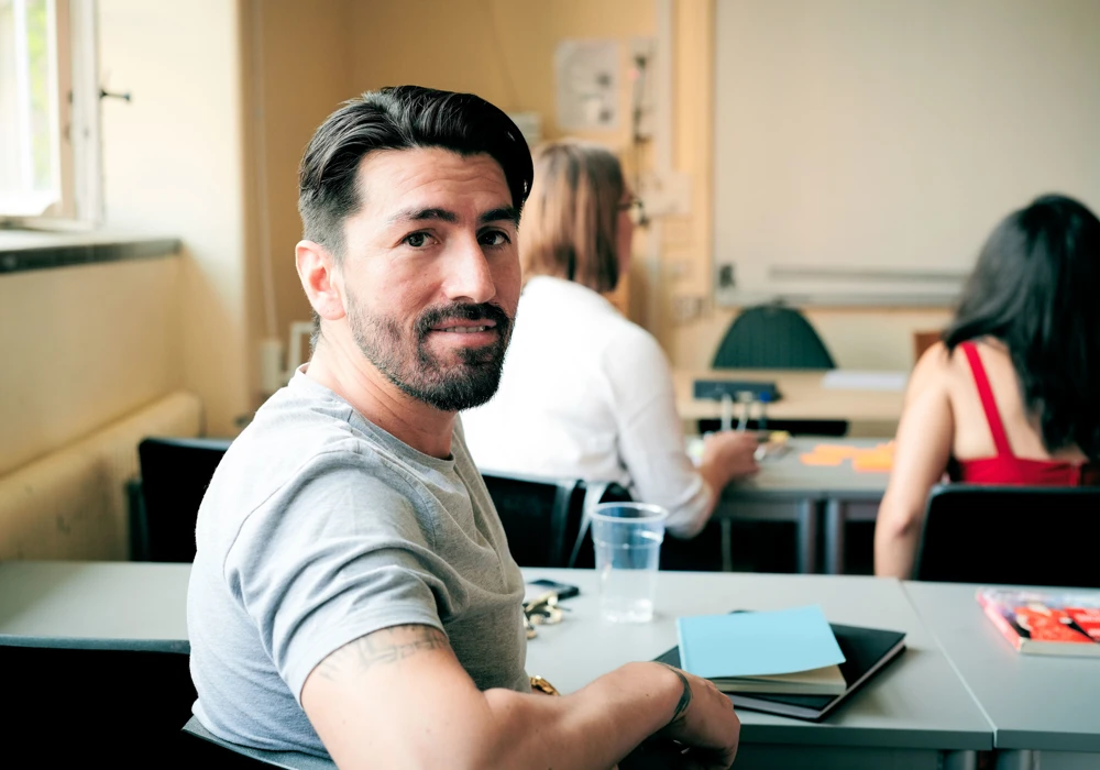 Man sitter vid skolbänk i klassrum.