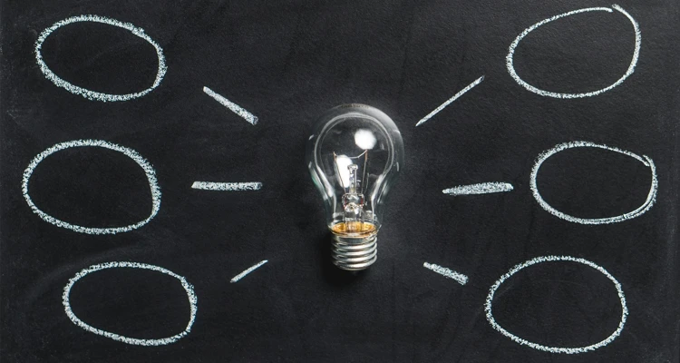 Glödlampa vid svarta tavlan, med idébubblor runtom.