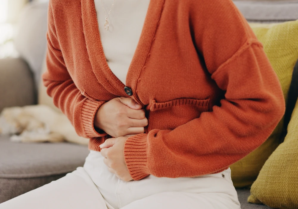 En kvinna håller sig om magen, på grund av mensvärk.