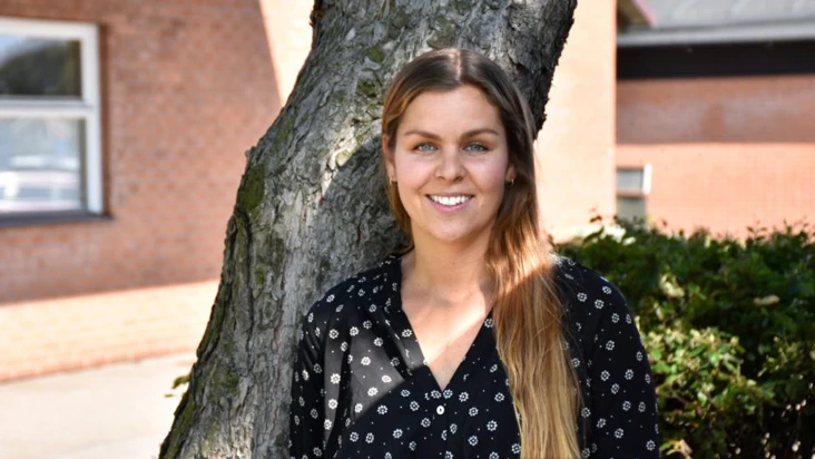 En kvinna st&aring;r bredvid ett tr&auml;d framf&ouml;r en byggnad.