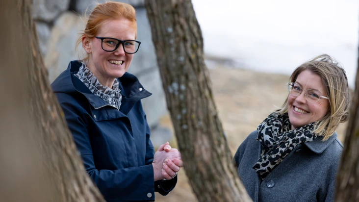 Tv&aring; kvinnor syns bakom grenar i ett tr&auml;d i kallt v&aring;rlandskap.