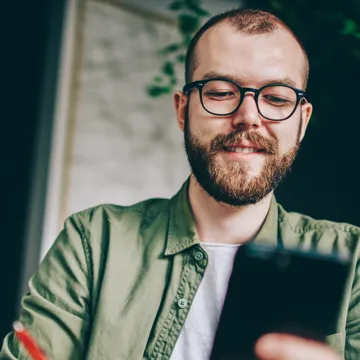 En man sitter vid ett bord och tittar p&aring; en mobiltelefon.