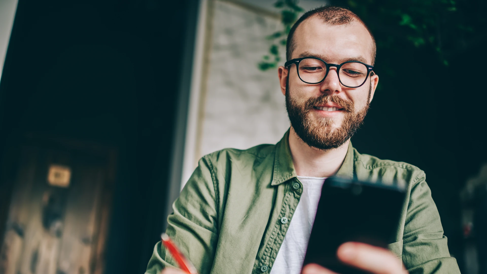 En man sitter vid ett bord och tittar på en mobiltelefon.