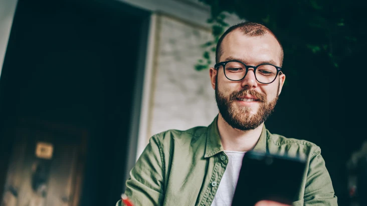 En man sitter vid ett bord och tittar p&aring; en mobiltelefon.