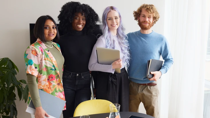 fyra personer, tre kvinnor och en man, st&aring;r tillsammans framf&ouml;r en svart sk&auml;rm i ett m&ouml;tesrum, med papper och datorer i h&auml;nderna.