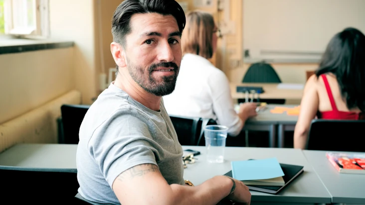 En man i gr&aring; t-shirt i skolb&auml;nk, v&auml;nder sig om och ser in i kameran.