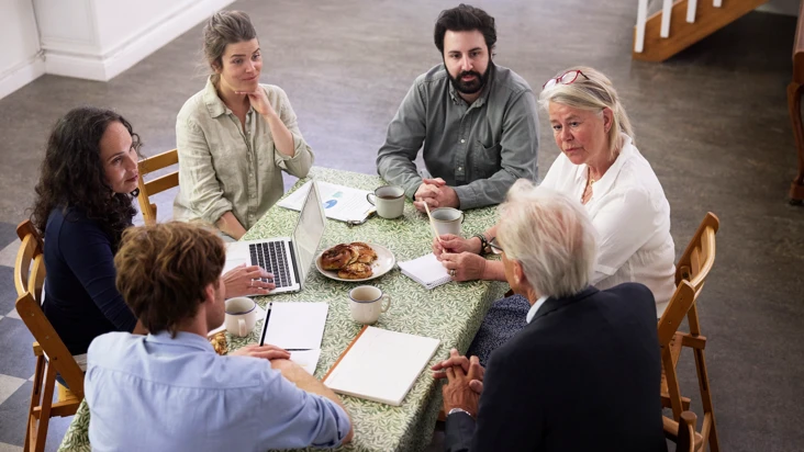En grupp m&auml;nniskor sitter runt ett bord och samtalar engagerat.