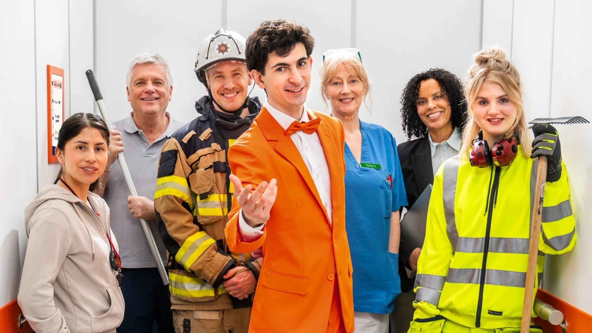 En grupp m&auml;nniskor med olika yrken st&aring;r i en hiss.