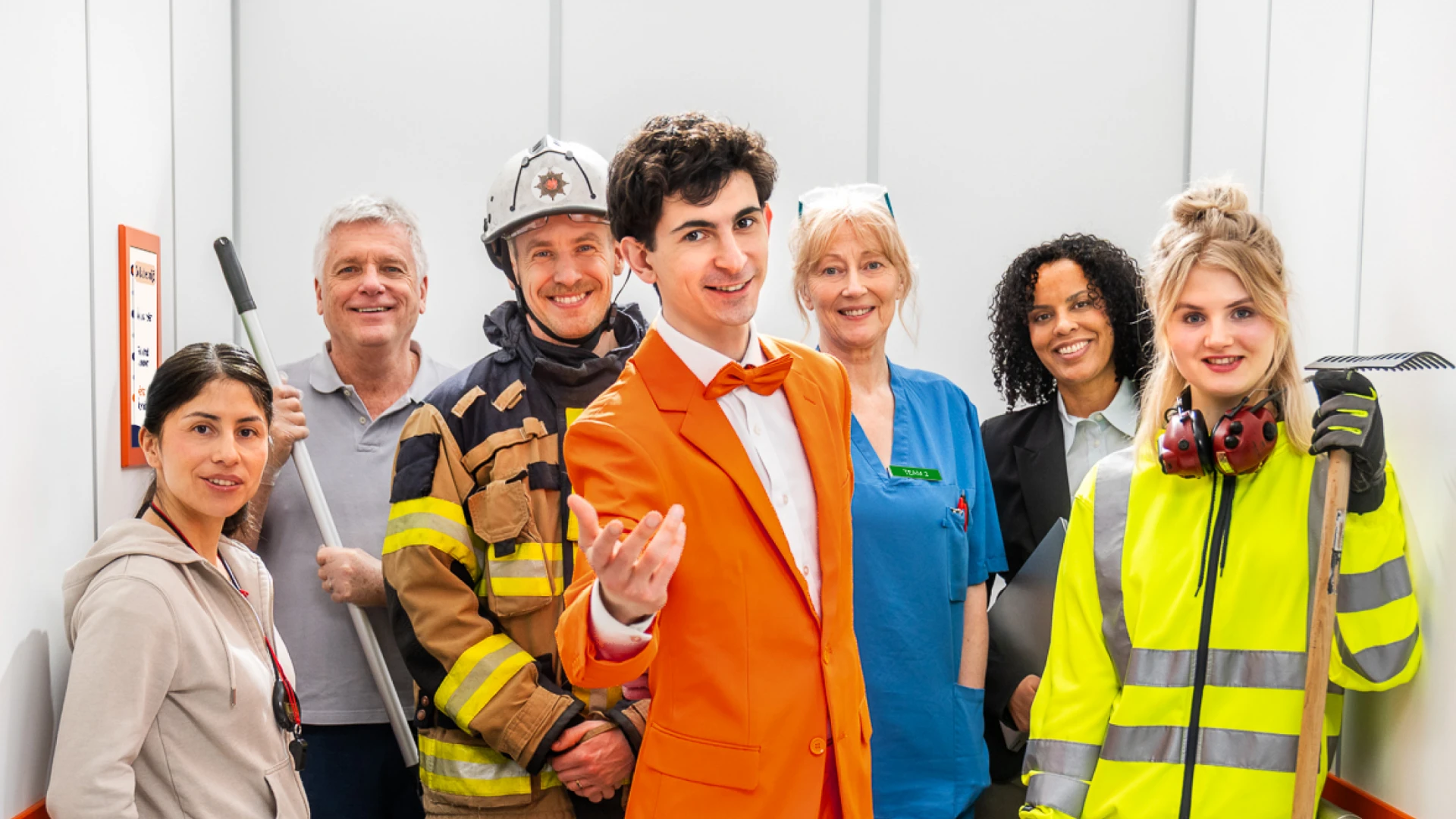 En grupp m&auml;nniskor med olika yrken st&aring;r i en hiss.