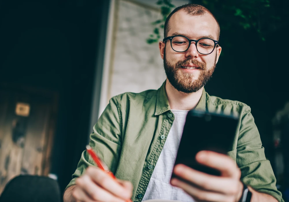 En man sitter vid ett bord och tittar på en mobiltelefon.
