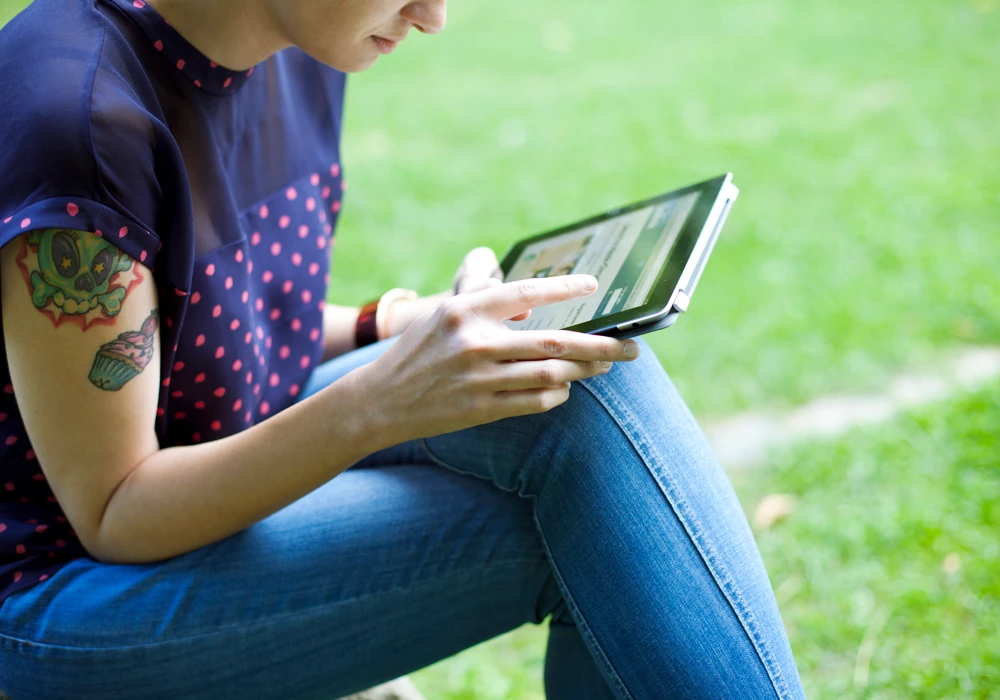 En kvinna sitter i gräset och använder en surfplatta.