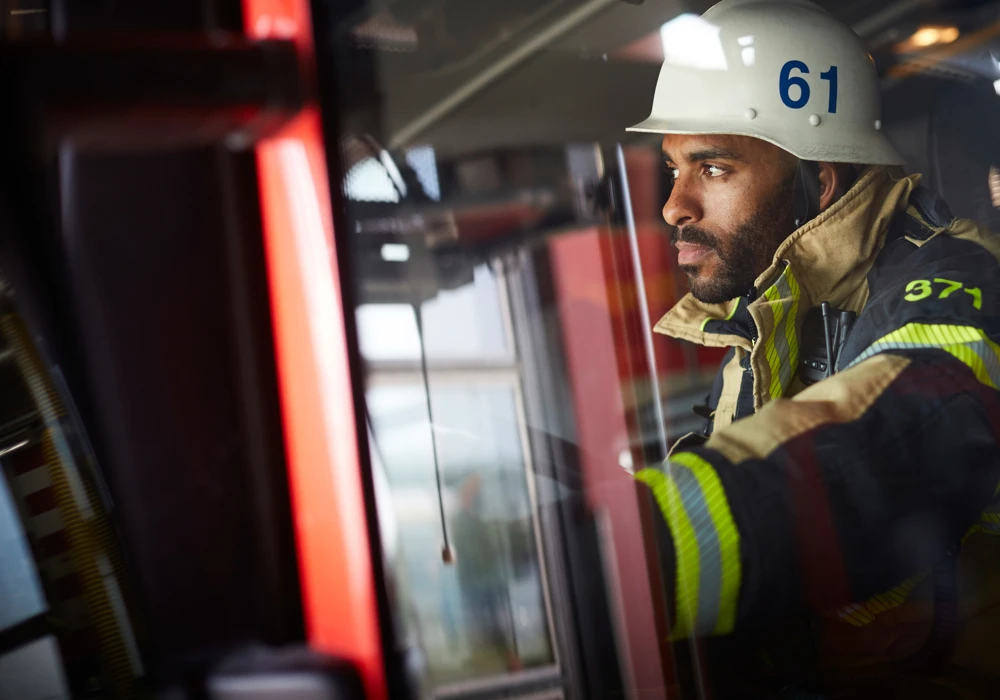 En man i brandmanskläder sitter i en brandbil och ser fundersamt ut genom rutan.