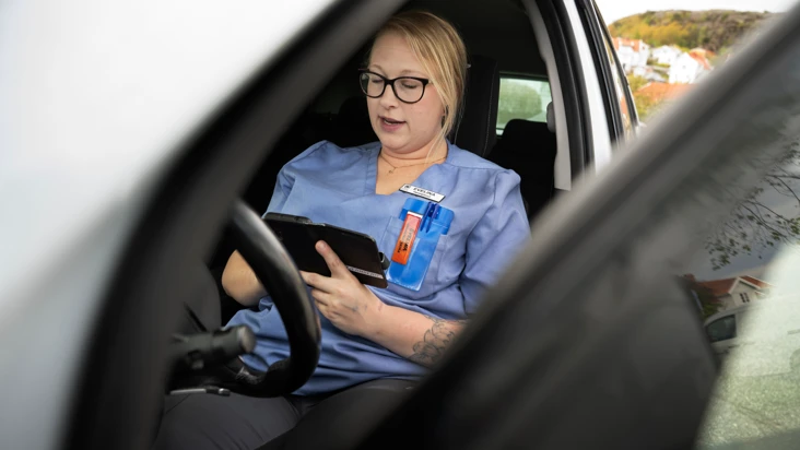 Kvinnlig undersk&ouml;terska sitter i vid ratten i en bil med &ouml;ppen bild&ouml;rr, och talar in i en mobil.