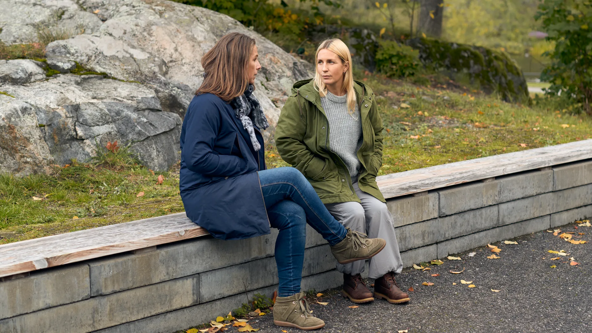 Två kvinnor sitter på en mur och pratar.