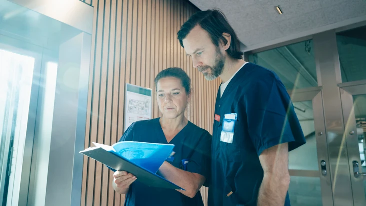 En man och en kvinna i operationskläder som tittar på ett skrivunderlägg.