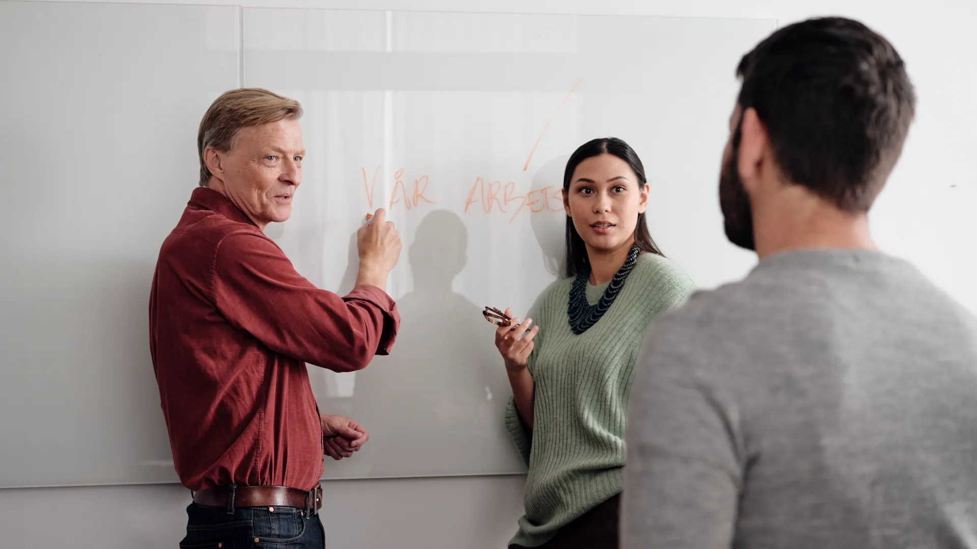 Tre personer står vid en whiteboard och pratar.